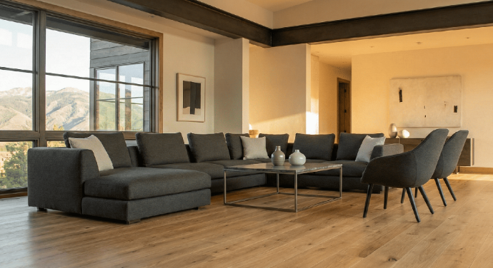 A spacious, modern living room featuring light-colored, wide-plank engineered wood flooring