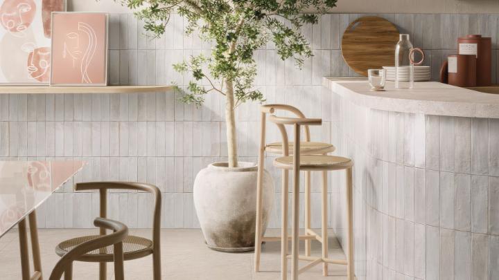 Cyprus Bianco 2x9 white ceramic subway tile installed in vertical stacked pattern on kitchen backsplash and island with natural light and modern bar stools