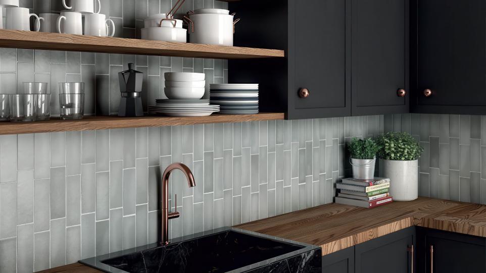 Kitchen sink area featuring a vertical Perfection grigio matte subway tile backsplash, open wood shelving, and a black marble sink with a copper faucet.