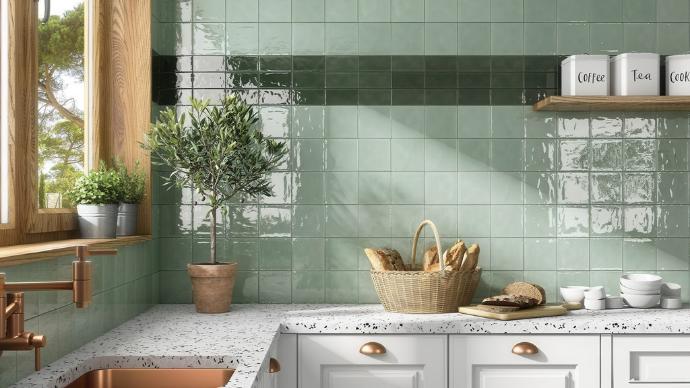 A glossy, square green subway tile kitchen backsplash with a dark accent stripe above a terrazzo countertop.