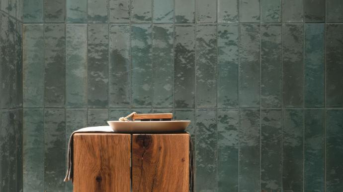 Rustic wooden stool in front of a wall of dark, glossy green Cyprus 2x9 Glossy Subway Tile.