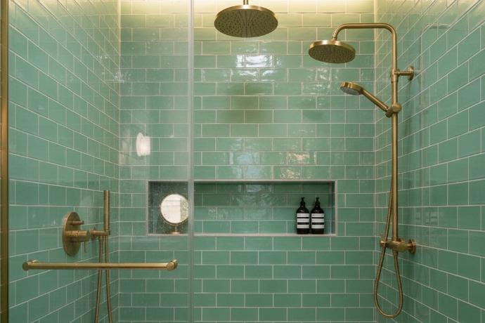 A modern bathroom shower with seafoam green subway tile walls and brass fixtures.