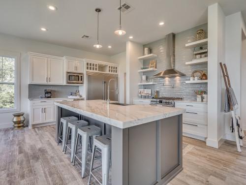 A modern kitchen with white cabinets, a marble island, and a light gray subway tile backsplash.