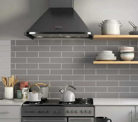 Kitchen with a grey glass subway tile backsplash, a dark range hood, stainless steel stove, and open wooden shelving displaying dishes and kitchenware.