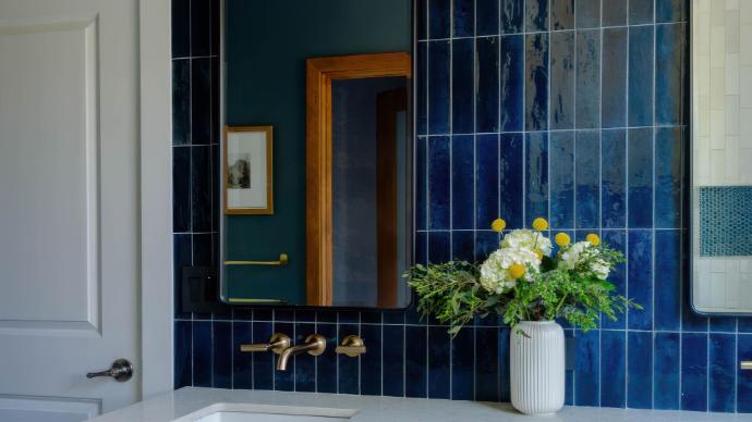 Bathroom vanity with glossy, vertically-stacked deep blue Cyprus subway tile, brass faucets, and a framed mirror.