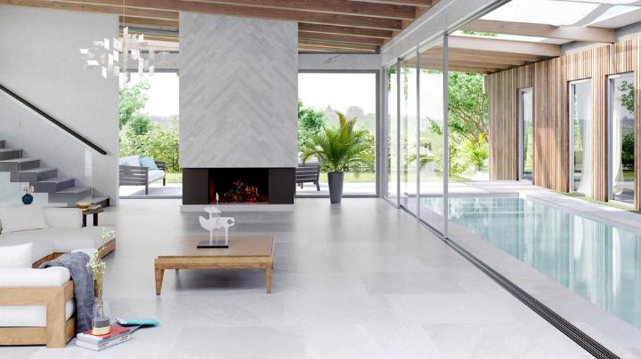 Modern luxury room with white flooring and an indoor pool, featuring a fireplace wall clad in Cardoso stone look porcelain tile in a herringbone pattern.