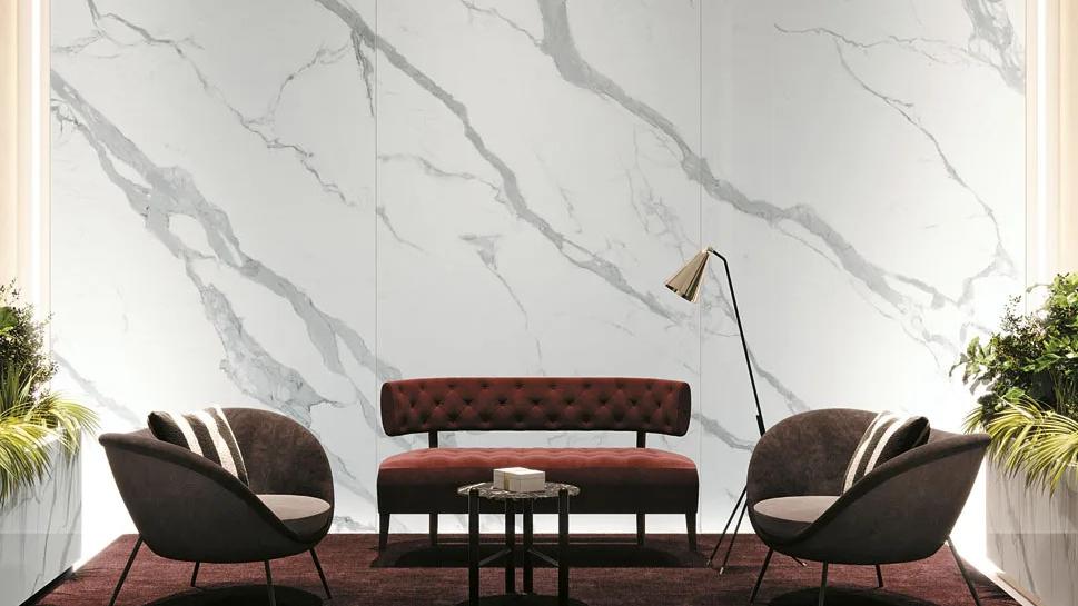 Stylish interior with Classic Statuario porcelain slabs, modern sofa, chairs, and greenery and floor lamp.