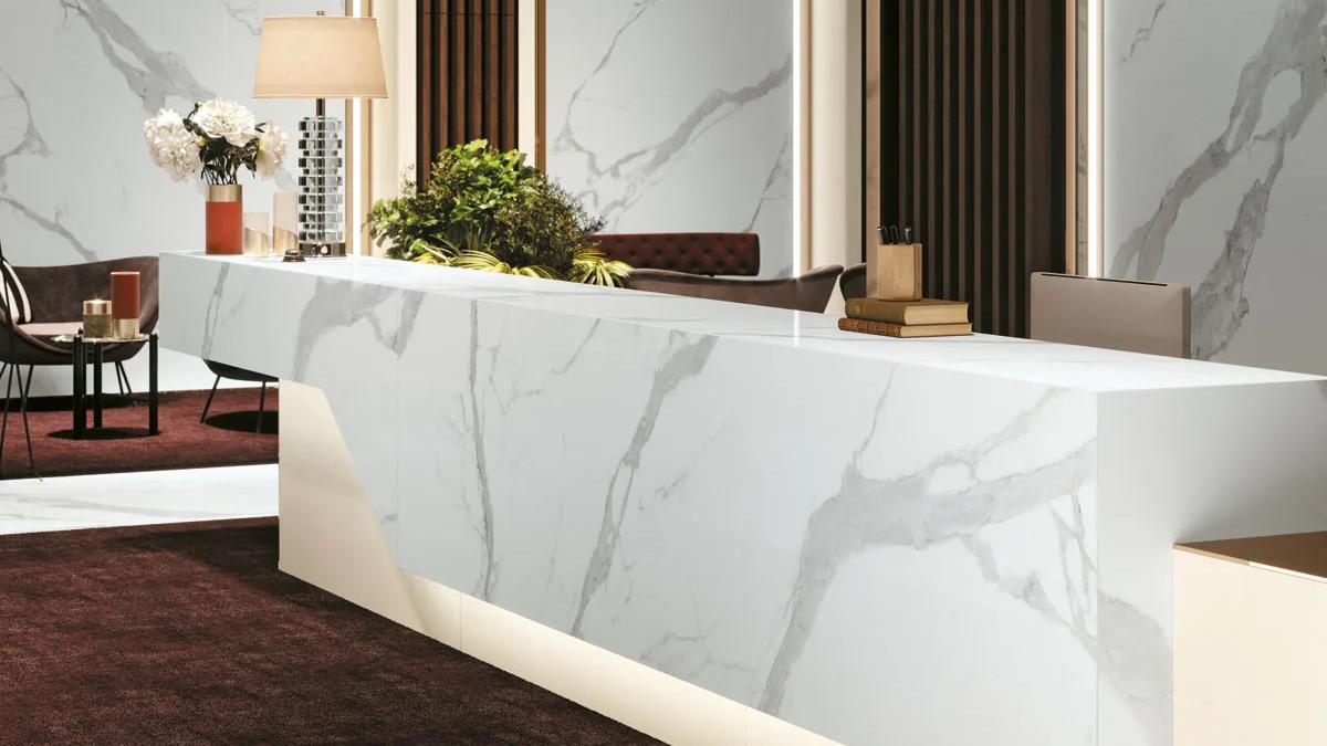 Hotel reception desk clad in Classic Statuario porcelain slabs with bold grey veining pattern.