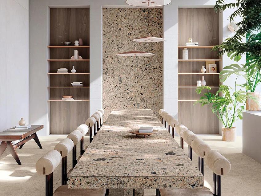 Long dining table made from Ceppo Romano porcelain slabs with cream chairs and wooden shelving.