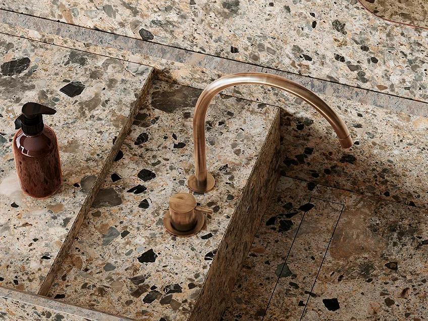 Bathroom sink detail showing Ceppo Romano porcelain slabs with integrated basin and copper faucet fixture.