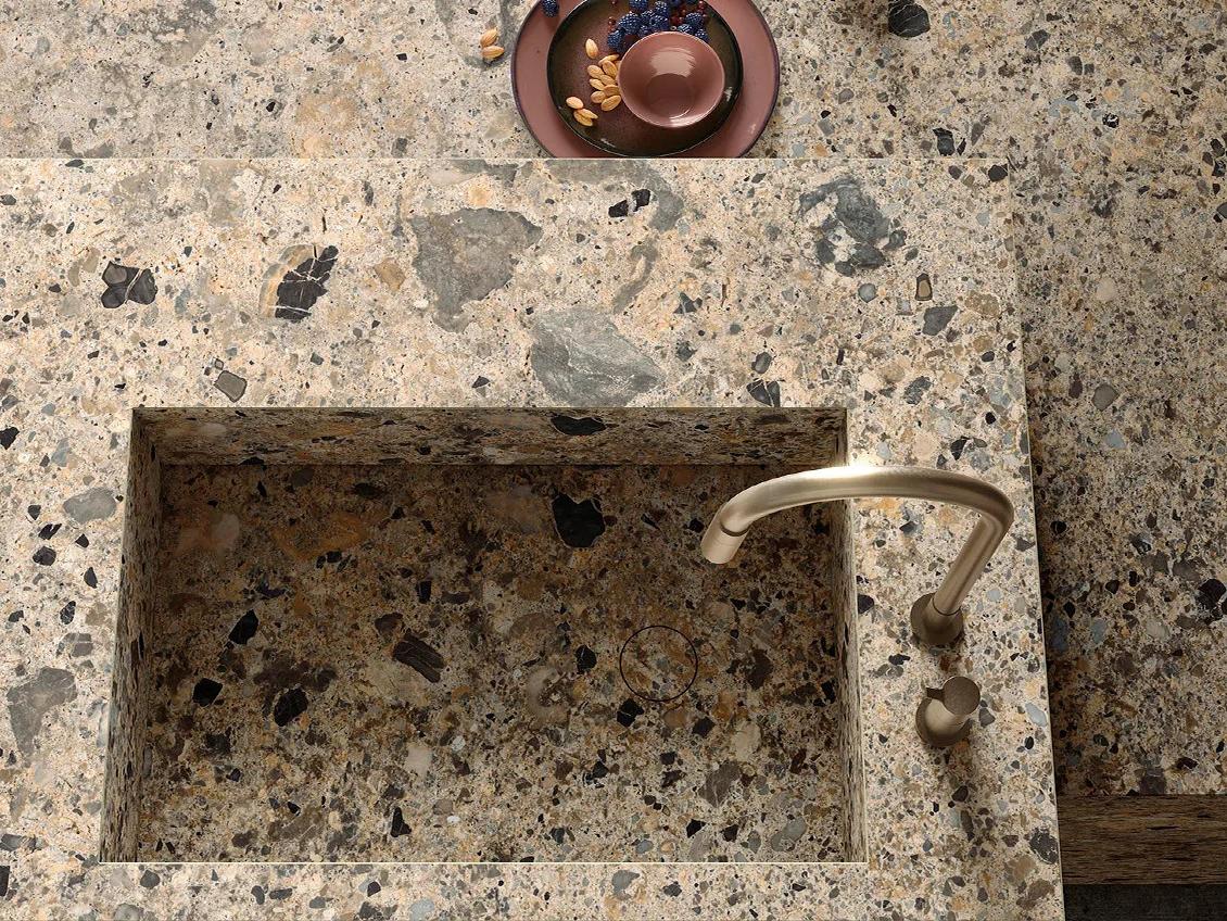 Kitchen sink carved from Ceppo Romano porcelain slabs with brass faucet and decorative dish styling.