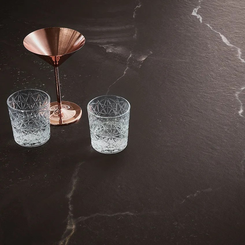Copper pitcher pouring water into crystal glasses on Andromeda porcelain slabs surface.