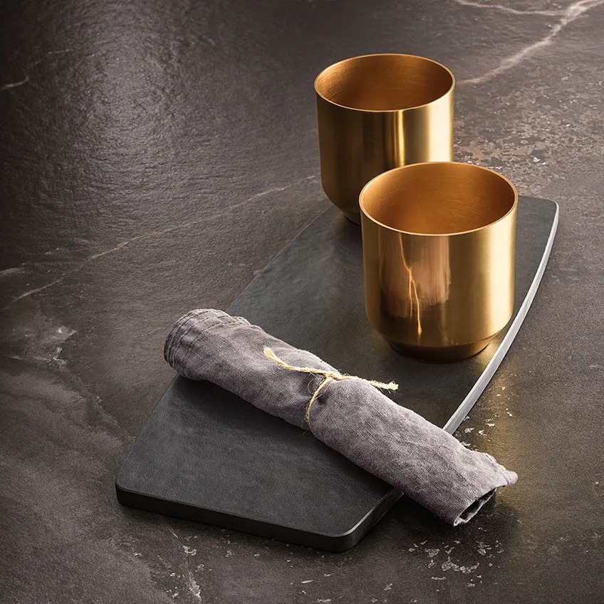 Gold cups and linen napkin on dark Andromeda porcelain slabs countertop surface.