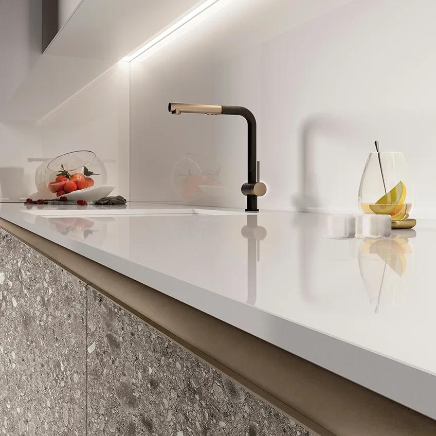 Modern kitchen countertop featuring Absolute White porcelain slabs with bronze faucet and fruits.