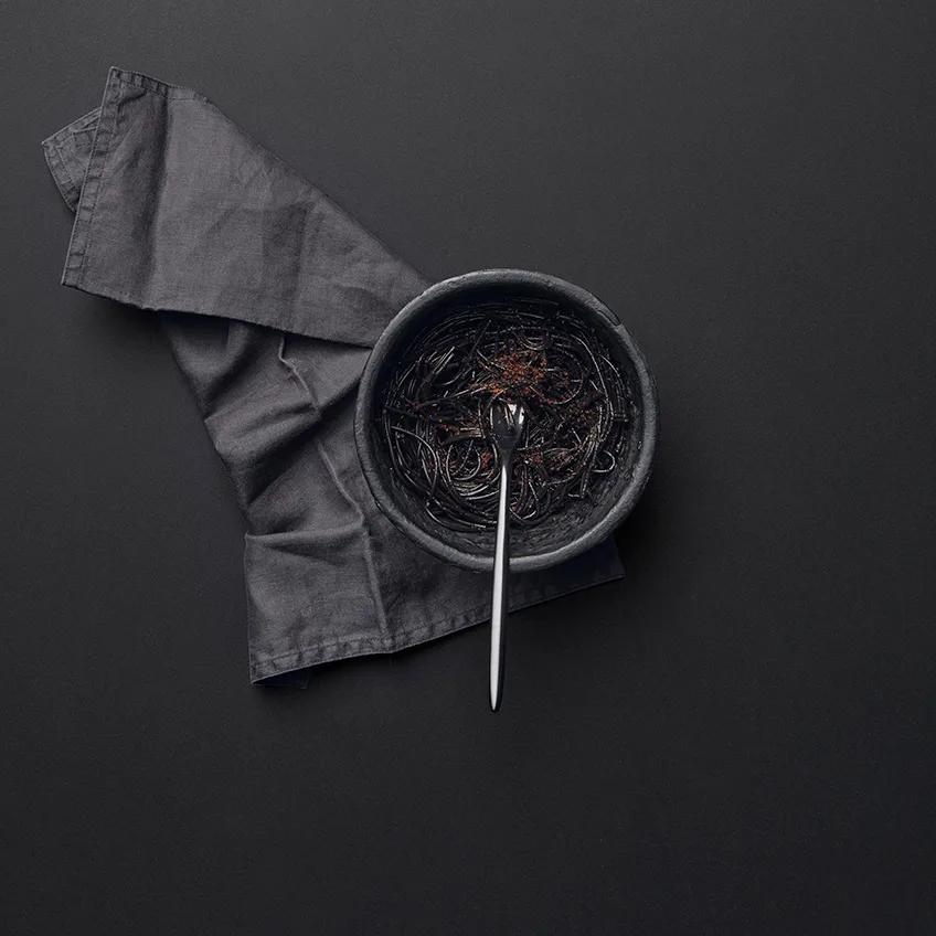 Absolute Black porcelain slabs surface with gray cloth napkin and ceramic bowl top view.