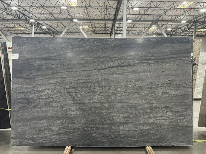 Full quartzite slab showcasing charcoal gray tones and flowing natural patterns Gray quartzite slab with natural wave-like veining displayed in stone warehouse