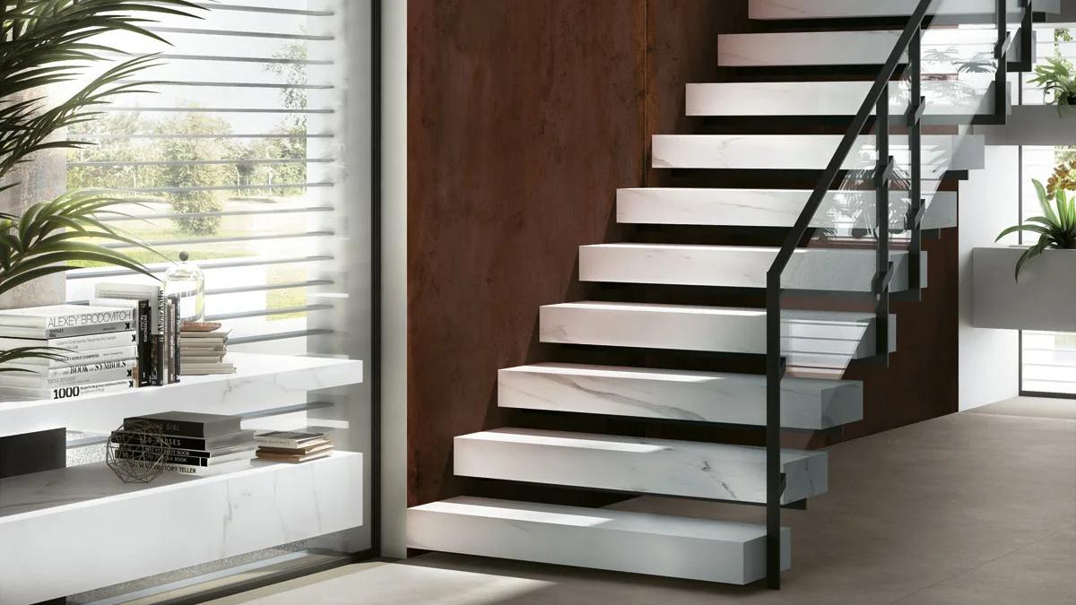 Floating staircase steps made from Extra Statuario porcelain slabs with dark metal railings.