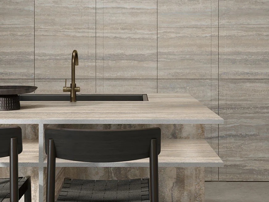 Kitchen island clad in Travertino Trilogy porcelain slabs with black chair and brass tap detail.